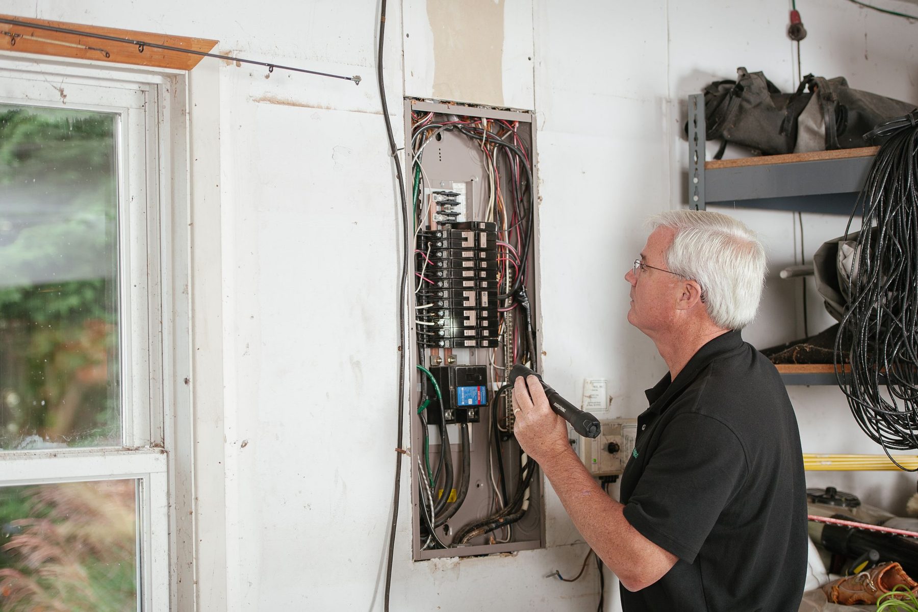 An electrician checking a residential breaker panel, used in the fictional Kestrel Electric concept
