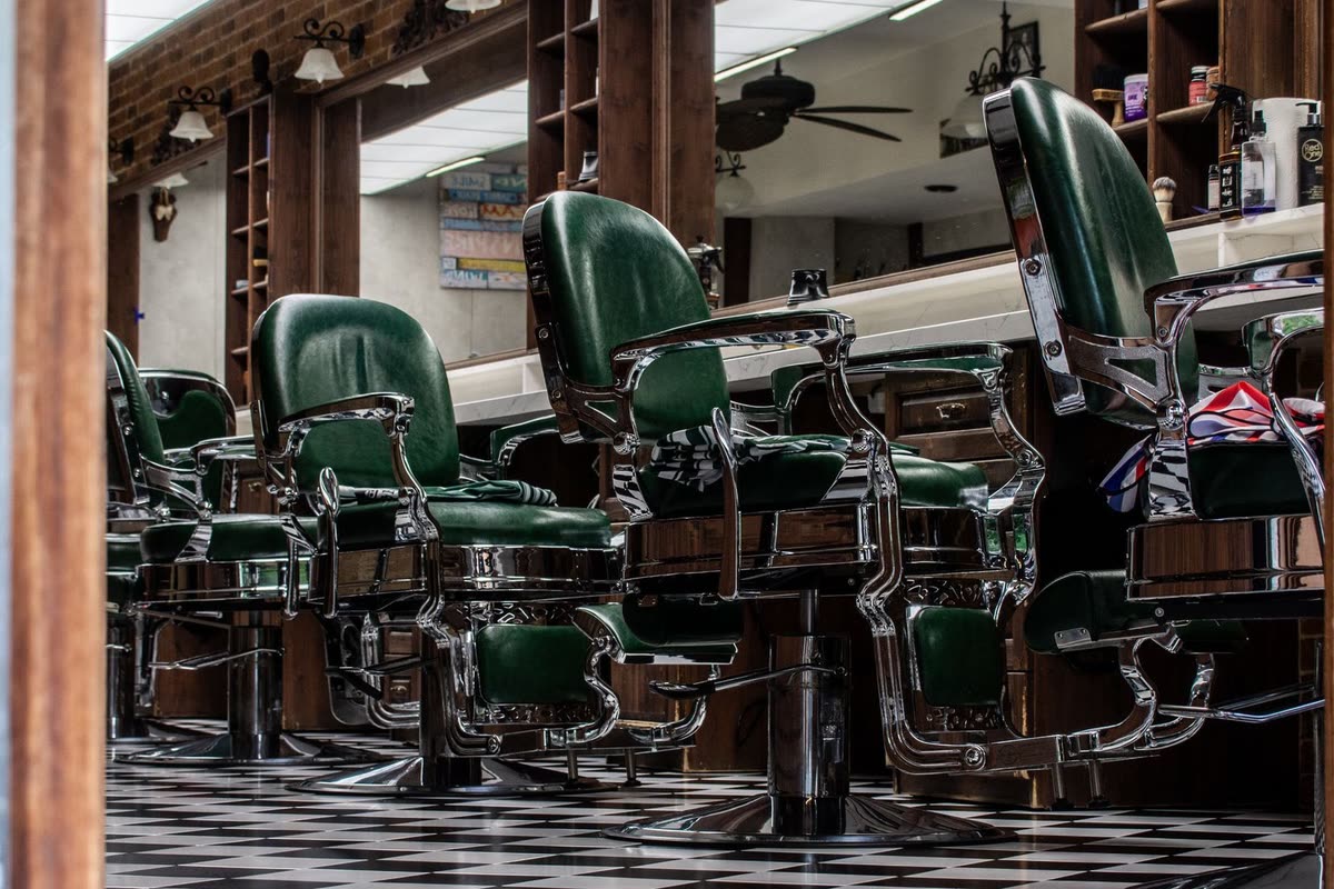 Green leather barber chairs on a checkerboard floor, used in the fictional Hollis Barbershop concept